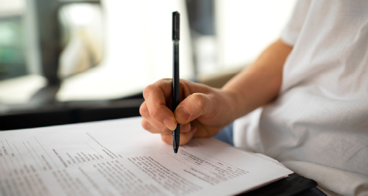 Fotografia de pessoa segurando lápis e respondendo questões de prova