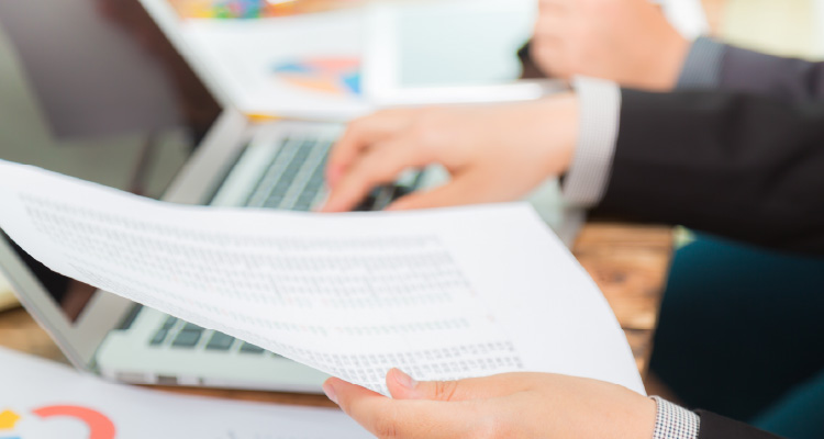 Imagem de pessoa digitando em notebook com papéis em uma mão