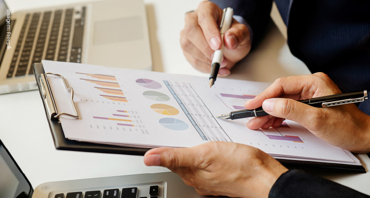 Fotografia de pessoas analisando papéis com gráficos e valores