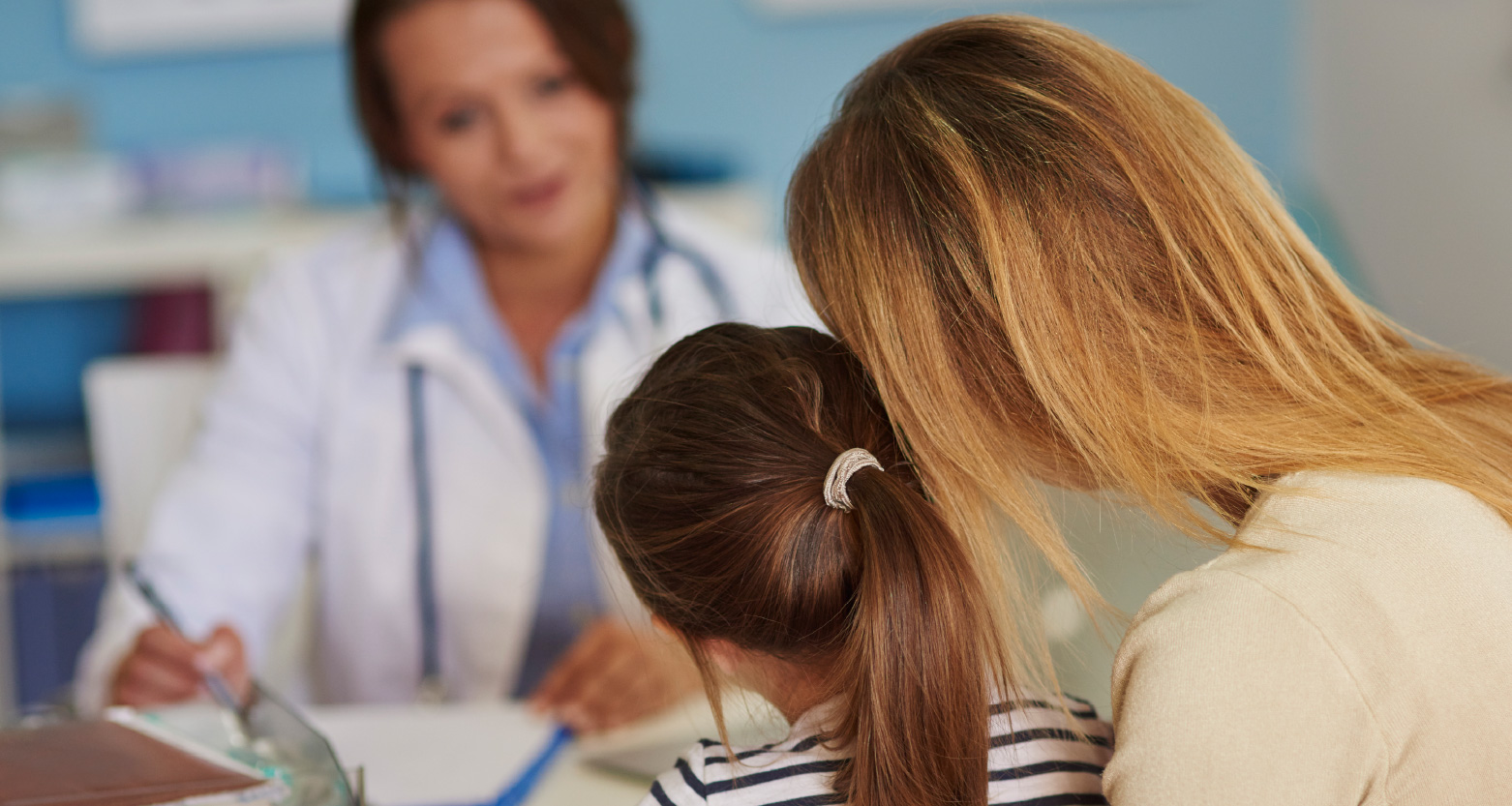 Fotografia de mãe e filha diante de médica em consulta